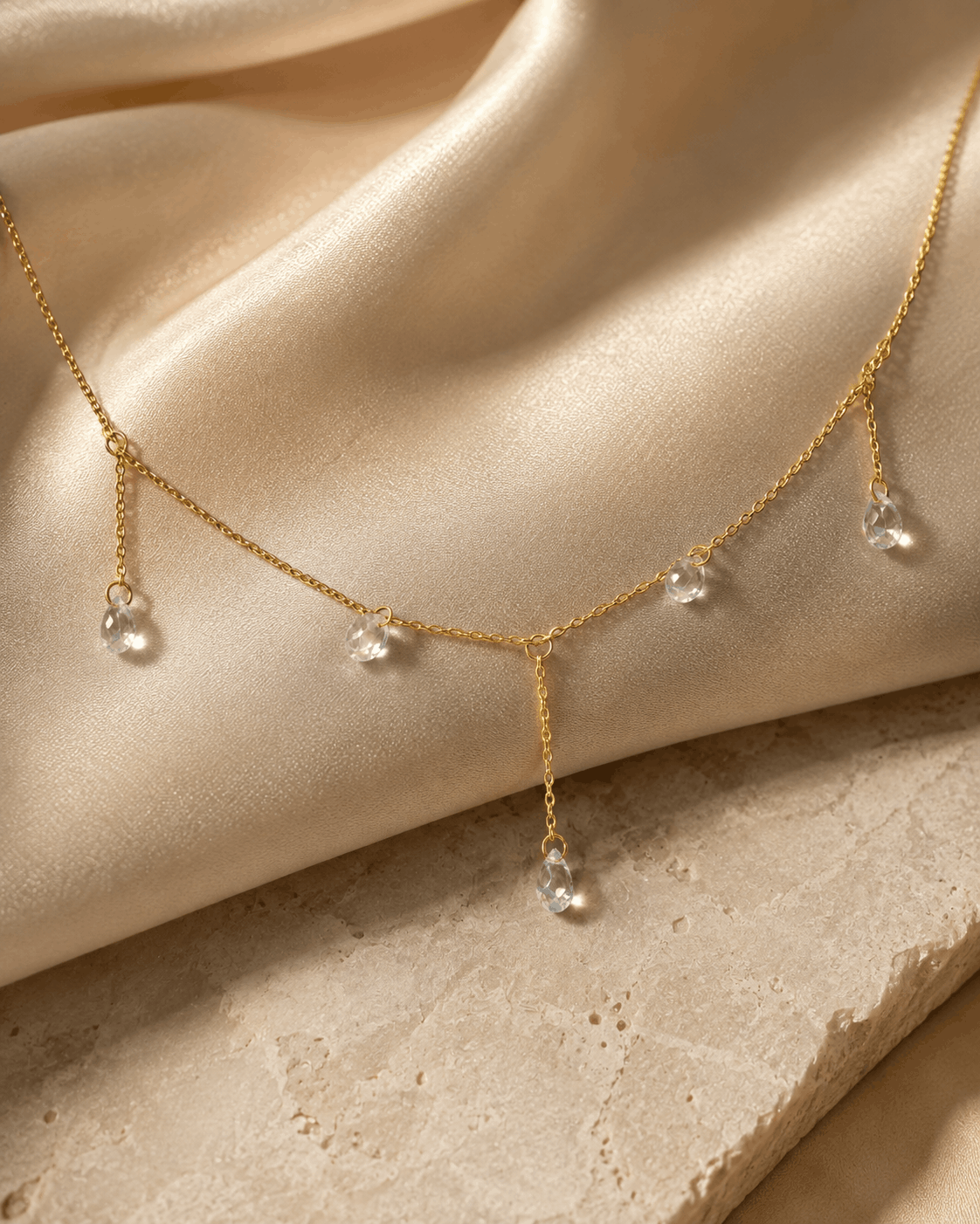 Celeste Glow gold-tone crystal drop necklace photographed on ivory satin