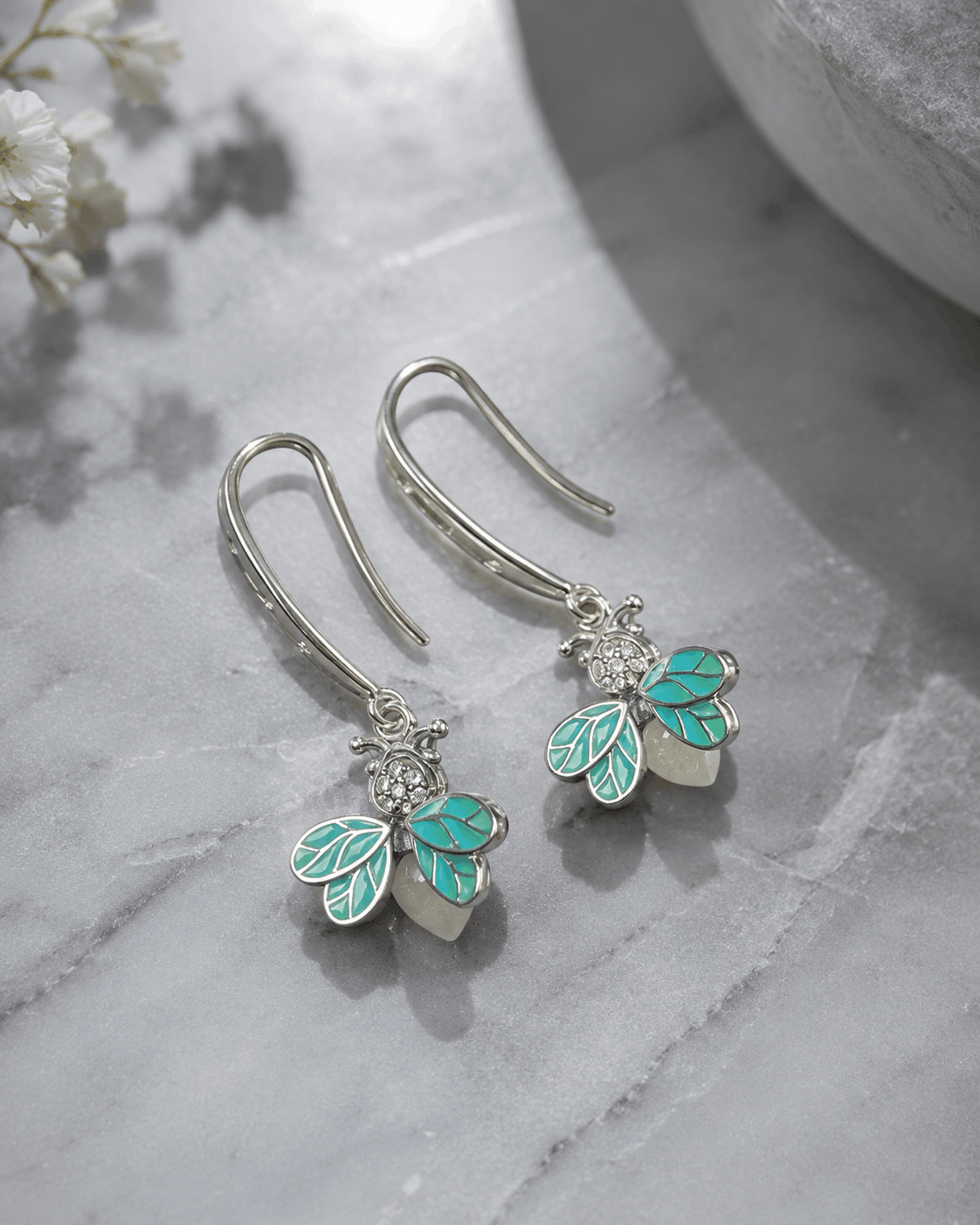 Turquoise Flutter silver-tone firefly drop earrings with turquoise enamel wings photographed on a natural stone surface