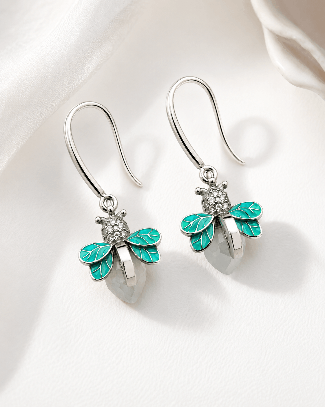 Turquoise Flutter silver-tone firefly drop earrings with turquoise enamel wings photographed on ivory satin