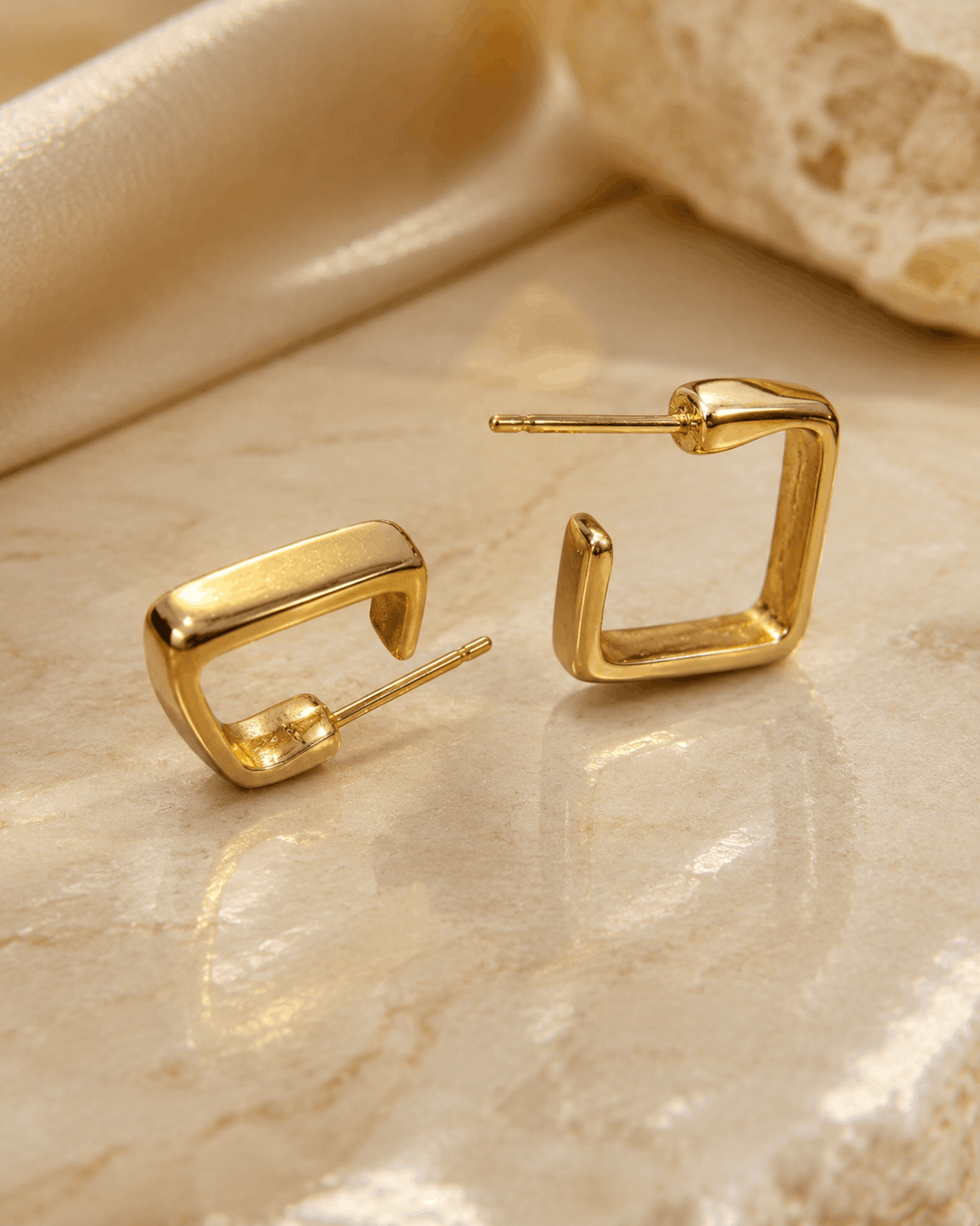 Modern Muse gold-tone square hoop earrings photographed on a natural stone surface