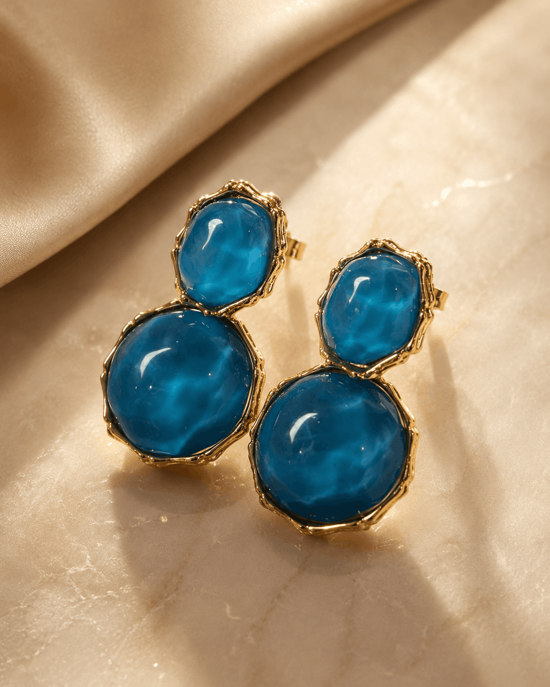 Azure Muse gold-tone earrings with blue resin stones photographed on gold satin