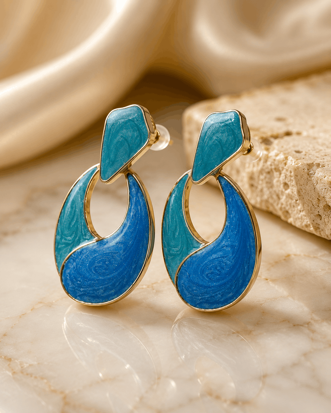 Ocean Muse gold-tone statement earrings with blue and teal enamel photographed on a natural stone surface
