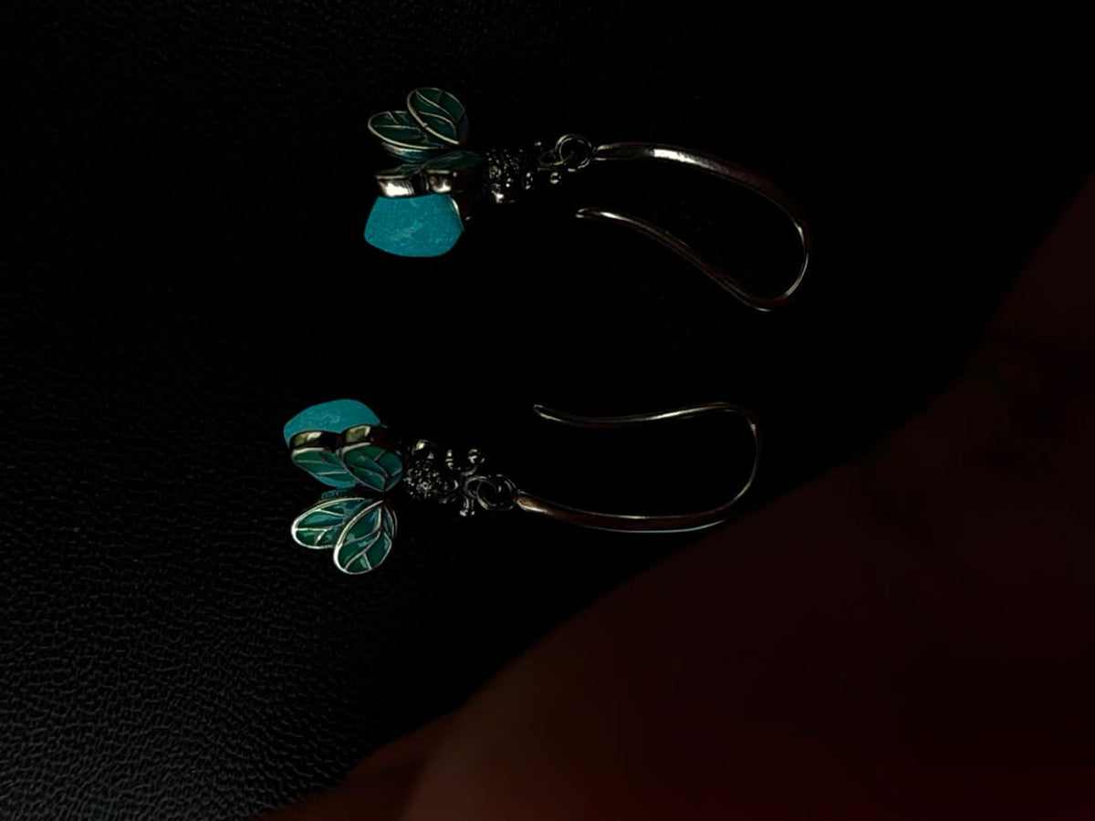 Turquoise Flutter silver-tone firefly drop earrings with turquoise enamel wings showing the glow-in-the-dark stone accent in low light